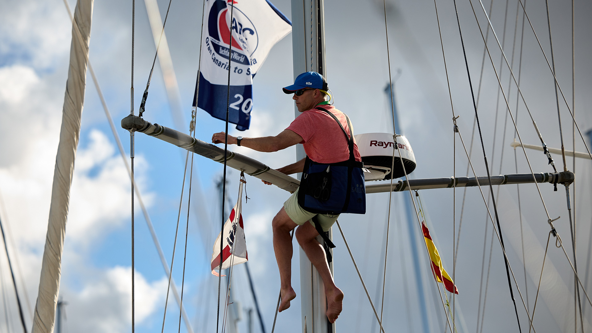 A man is up the mast of an ARC yacht in a bosuns chair taping the spreaders