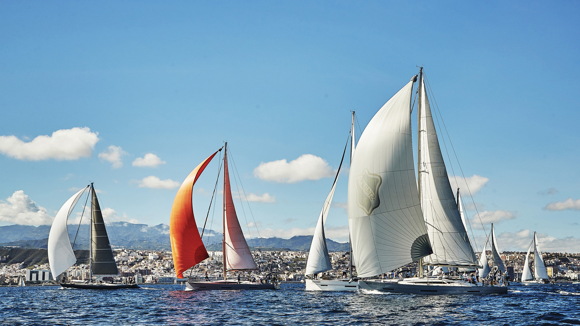 The start of ARC 2018 with yachts flying colourful sails with the city of Las Palmas in the background