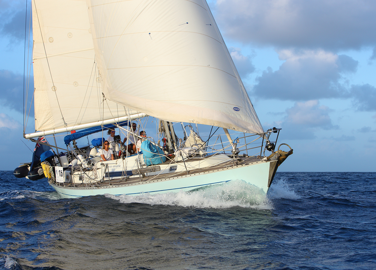 Pale blue yacht Penny Oyster with white sails and a bow wave finishes ARC 2023