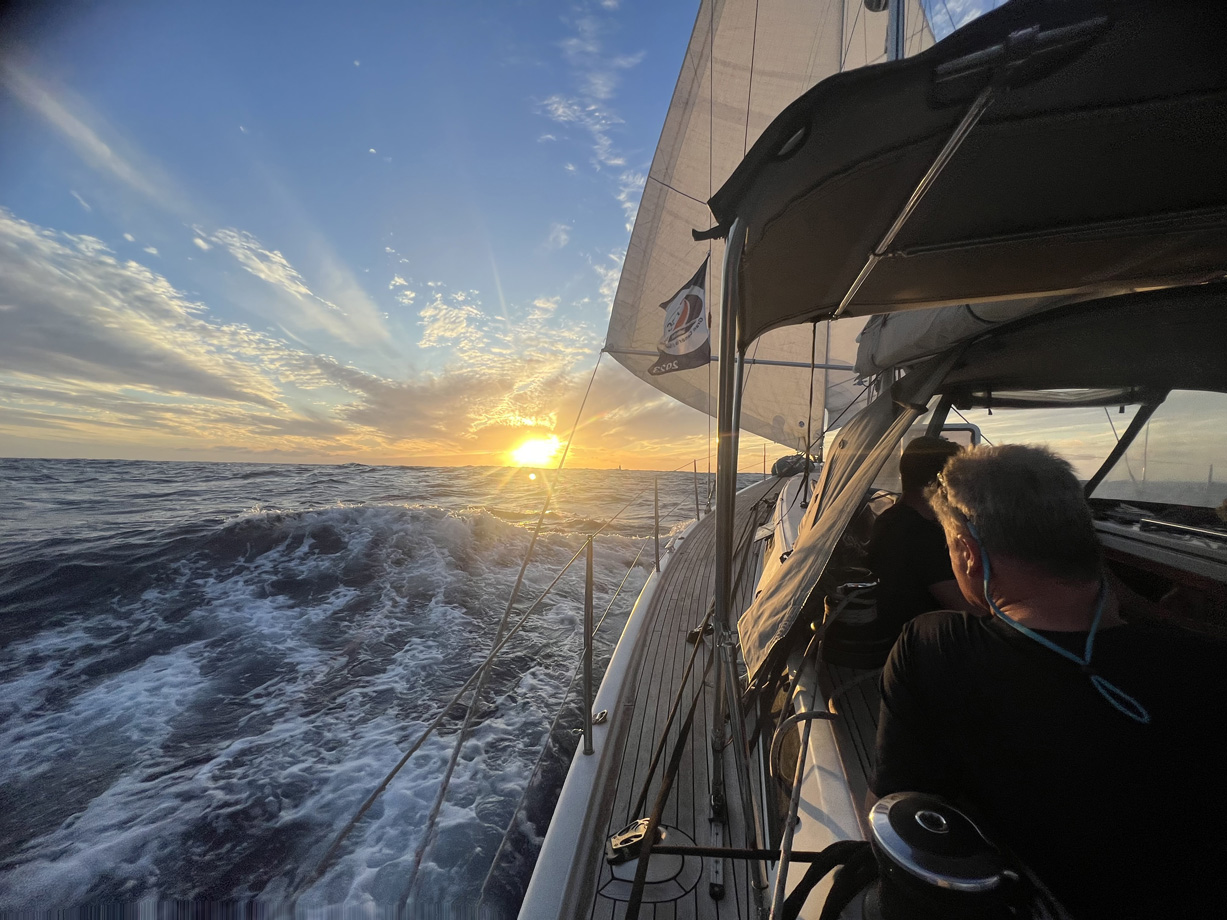 A crew man watches the sunset from the cockpit of yacht Flying in the middle of the Atlantic