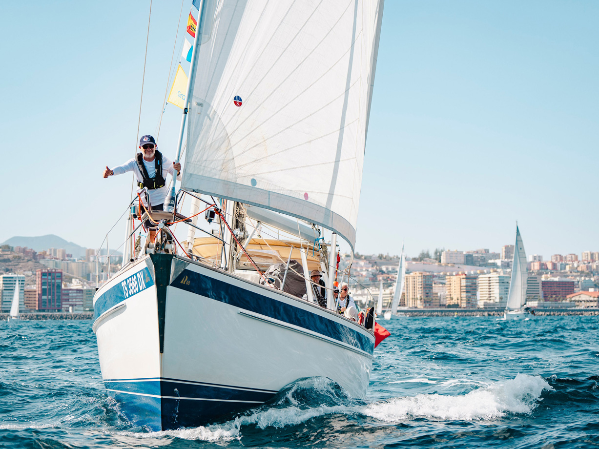 Hallberg Rassy yacht Aleide with a crew member giving a thumbs up on the bow at the start of ARC Plus 2024 in Las Palmas