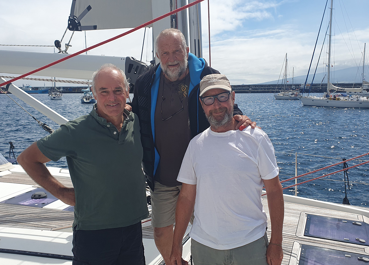 The three man crew on the deck of yacht Mojo in Horta harbour in ARC Europe 2025