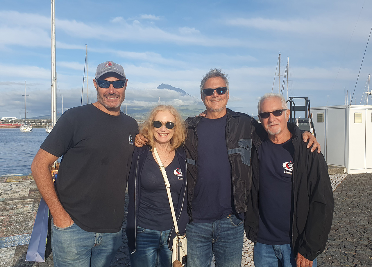 Three men and a woman from ARC Europe yacht Luna smile in the sun on Horta sea wall