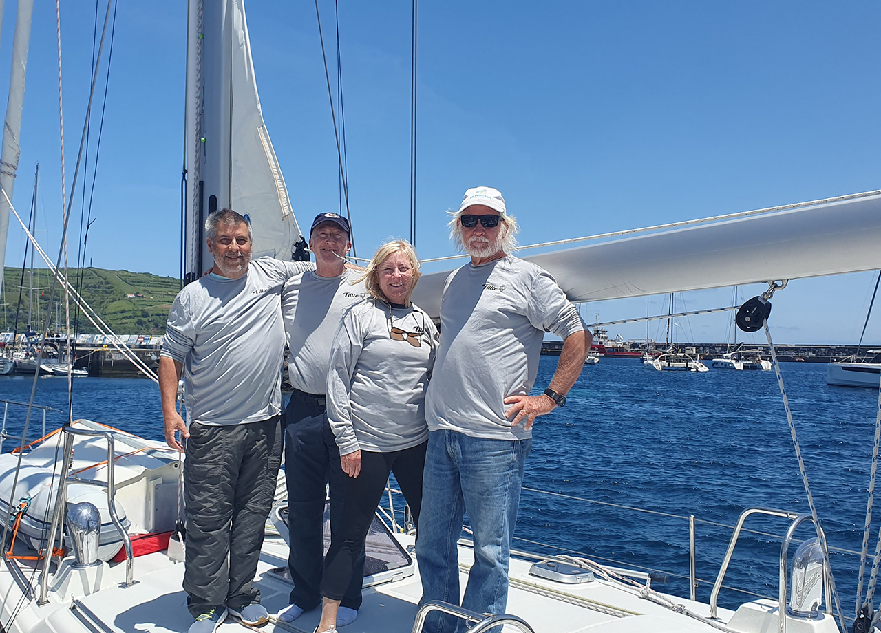 Three men and a woman stand on the deck of yacht Tillie on a sunny day in Horta, Azores as part of ARC Europe