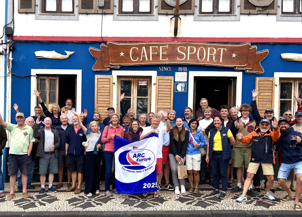 All the ARC Europe 2025 crews stand infront of the famous Peter Cafe Sport in Horta, Faial, Azores holing the rally flag