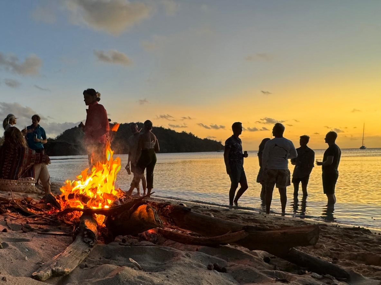 A bonfire busrns on a beach as party goers are silhouetted against the sunset in Fiji