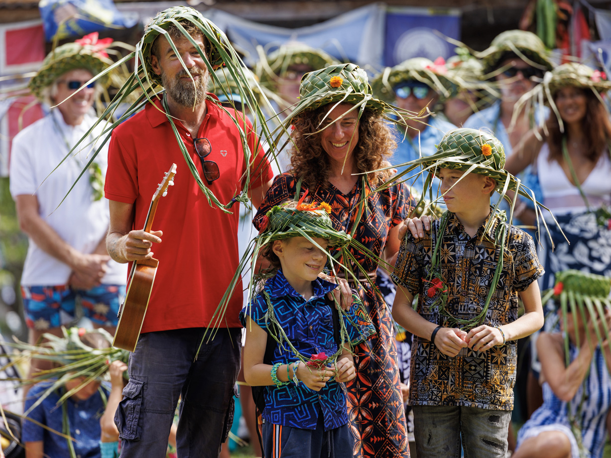 Men, women and children wear green palm frond hats and hold ukeleles