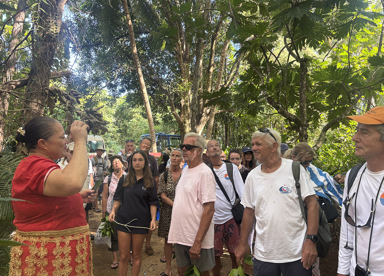 A woman in Tongan costume explains the plants and ecology of Tonga in a wooded area of the botanic garden