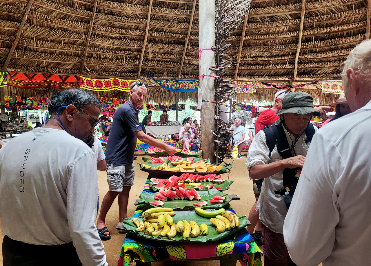 A buffet feast is laid out on banana leaves in a large wood and palm Embera building