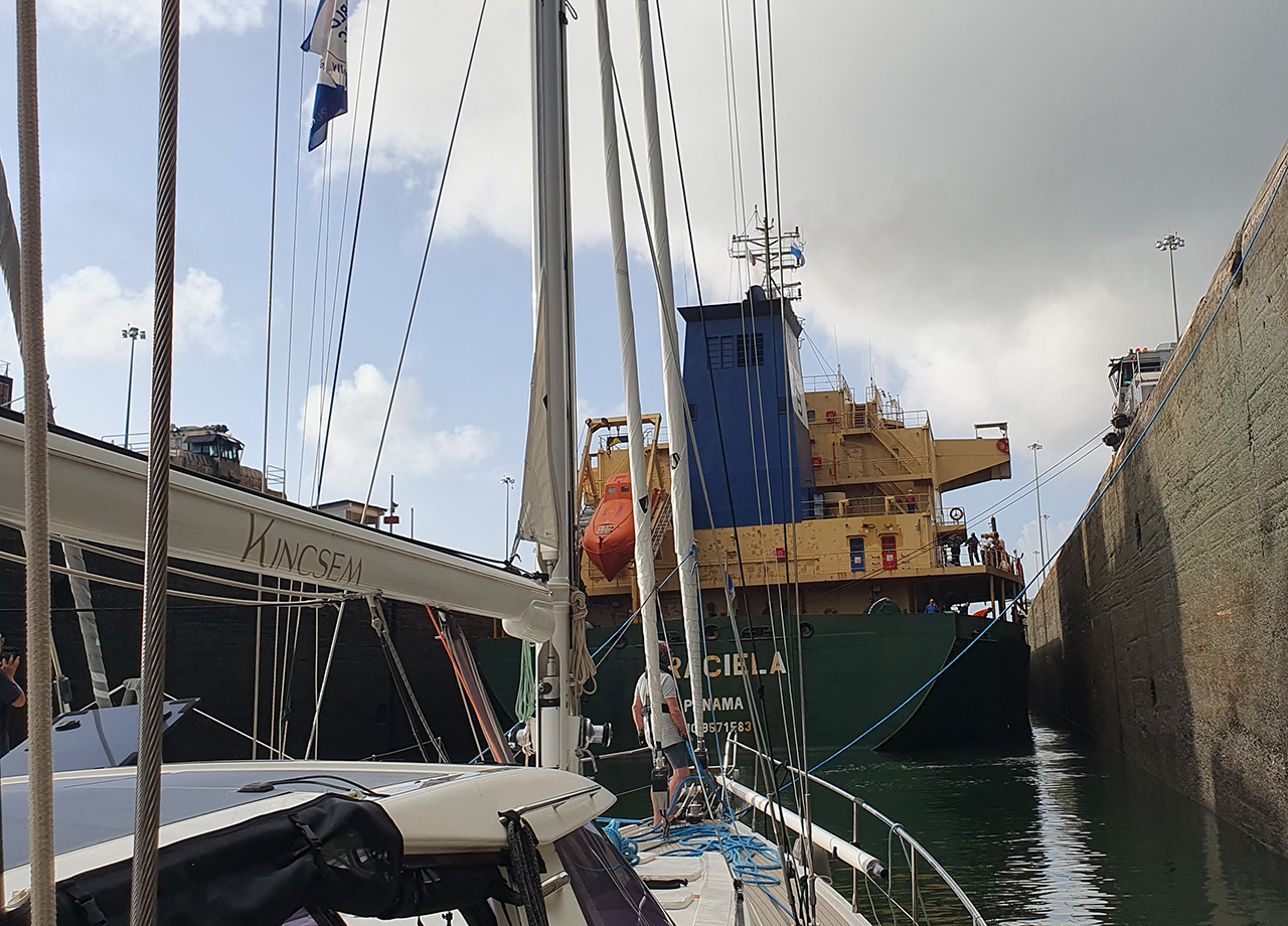 A sailing boat in a lock in the Panama Canal behind a large ship.