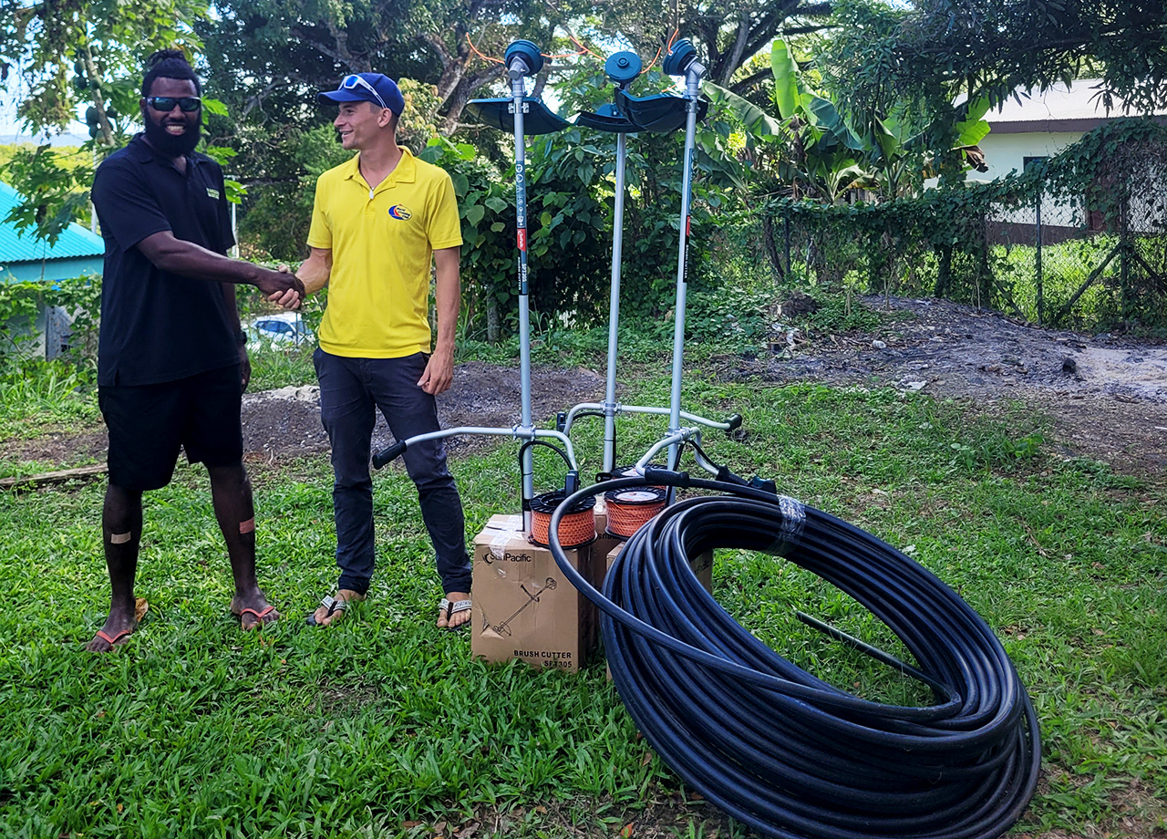 A man wearing a yellow shirt shakes hands with a black man with a coil of hose in the foreground