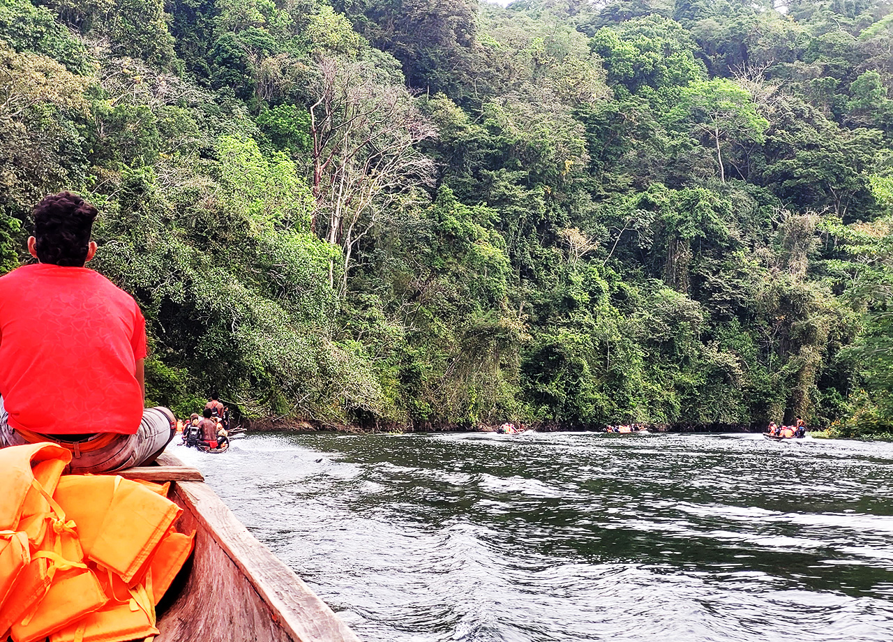 Wooden longboats follow each other up a river through dense forest in Panama
