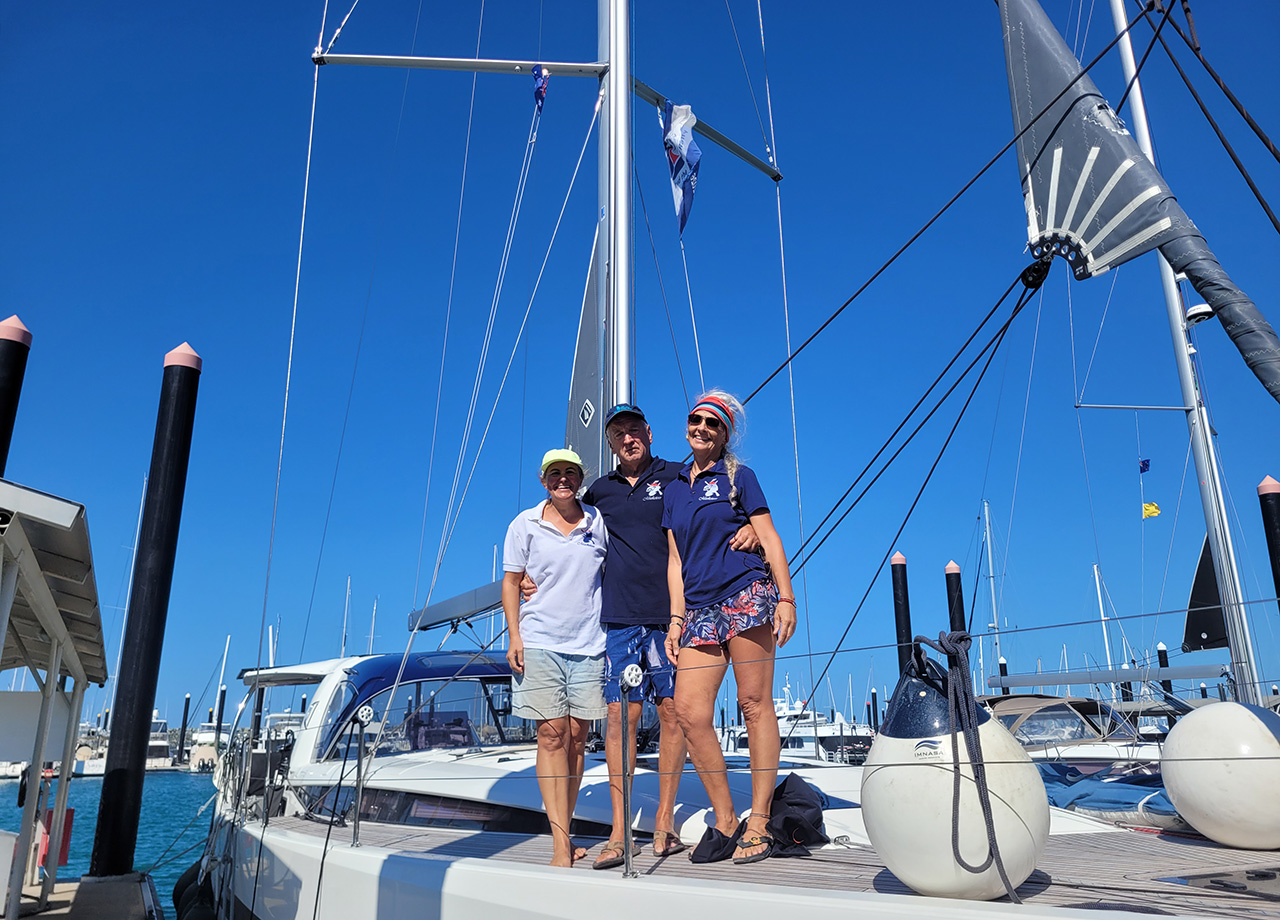 Two men and a woman stand on the deck of yacht Musketeer in the sunshine in Mackay