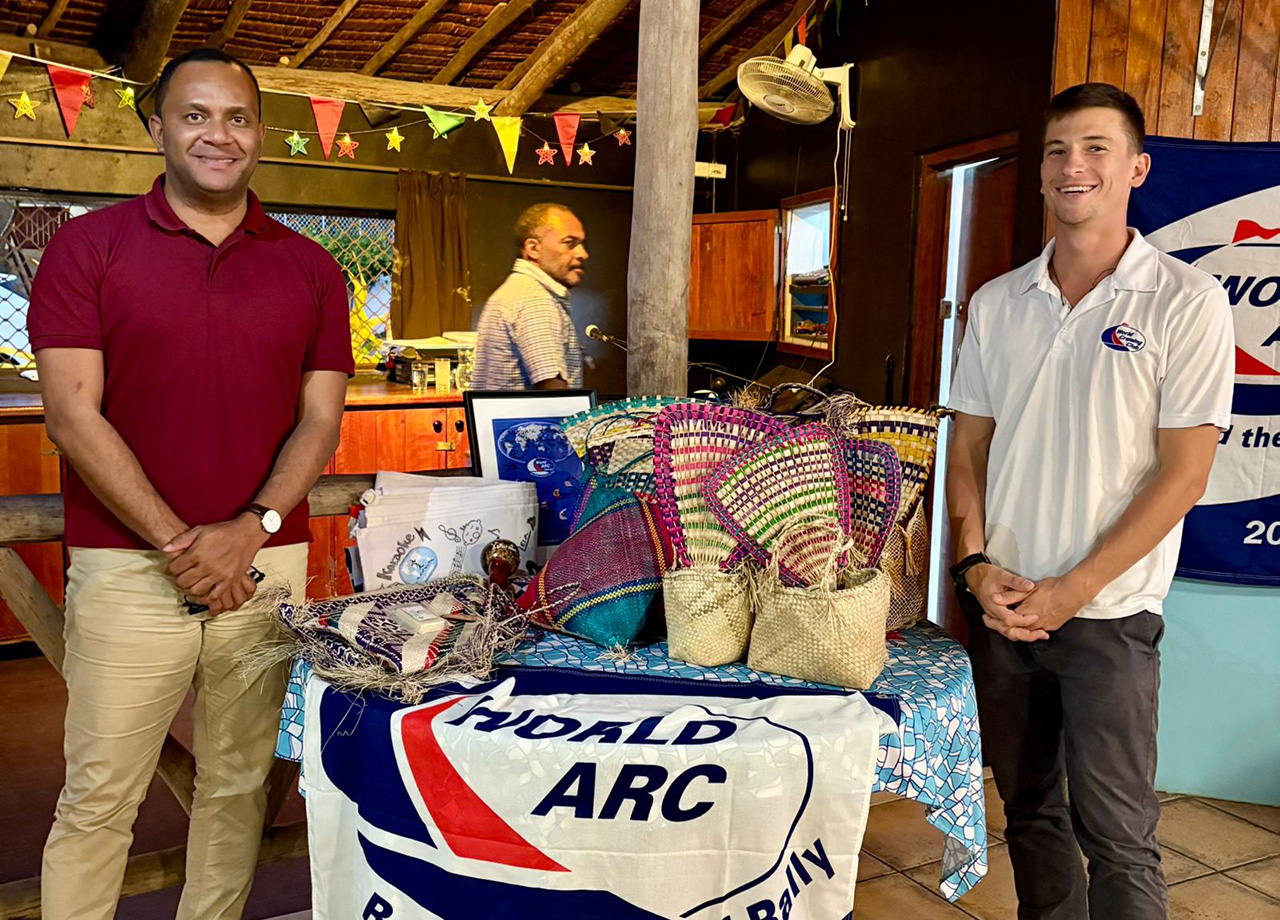Two men pose beside a table bearing local prizes and covered in the World ARC flag
