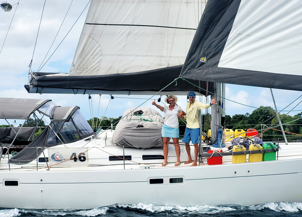 A man and a woman wave from the deck as yacht Salinity sails by
