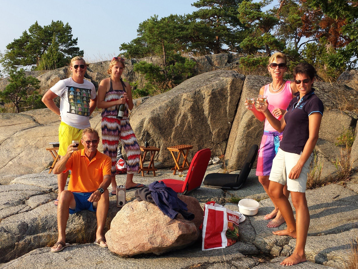A group of five men and women wearing bright clothes having a picnic on a smooth rock with pine trees in the background