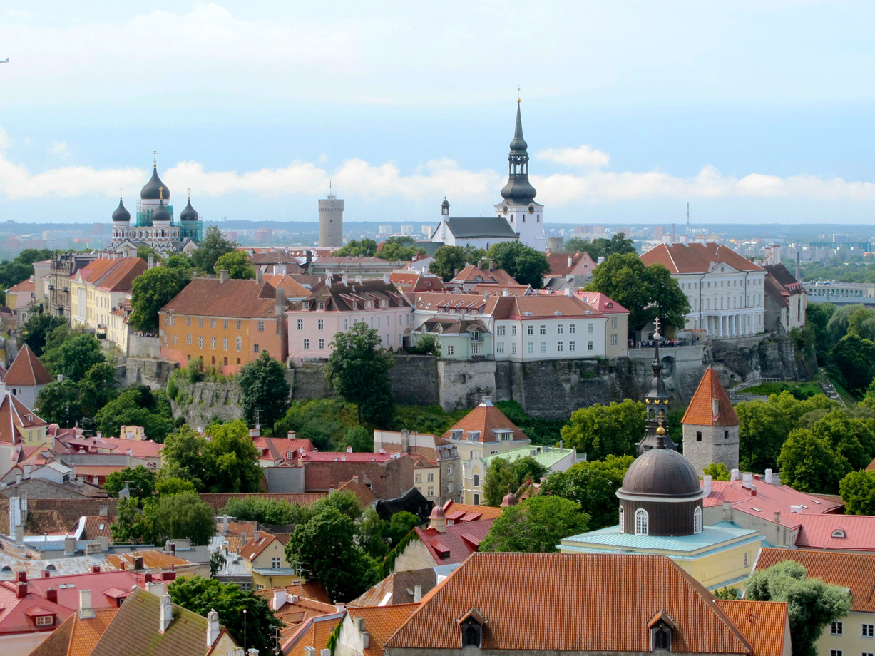 The city of Tallinn with red tiled roofs and yellow, pink and white historic buildings and two large churches with green spires and domes