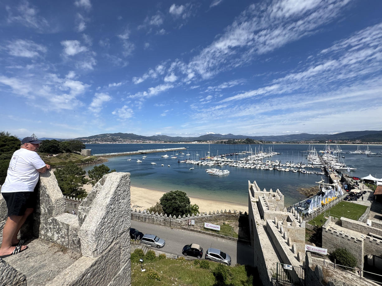A man leans against the wall of the fort in Baiona overlooking yachts moored in the marina