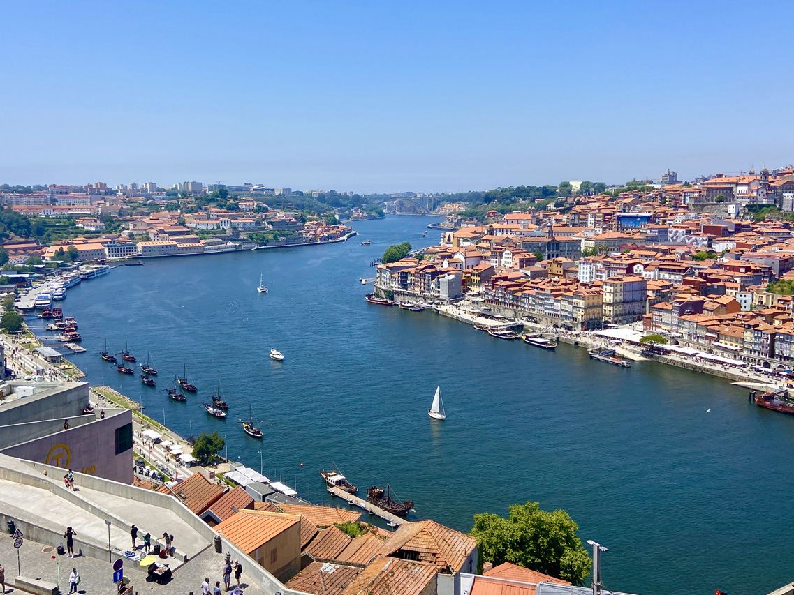 Looking down onto the river Duoro in Porto with the red roofs of the city and a yacht sailing on the river