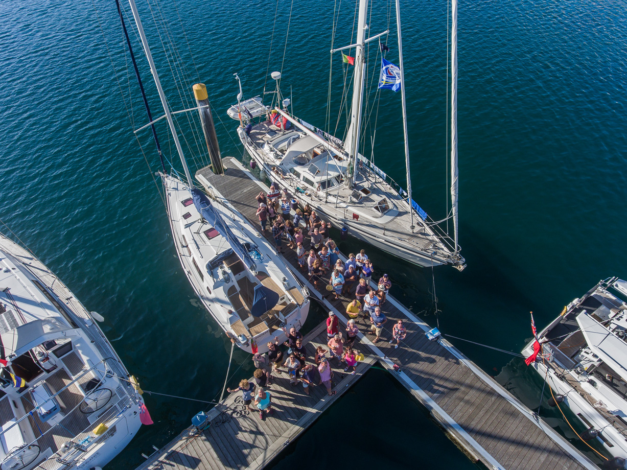 An aerial view of lots of people on a marina dock with boats moored to the dock