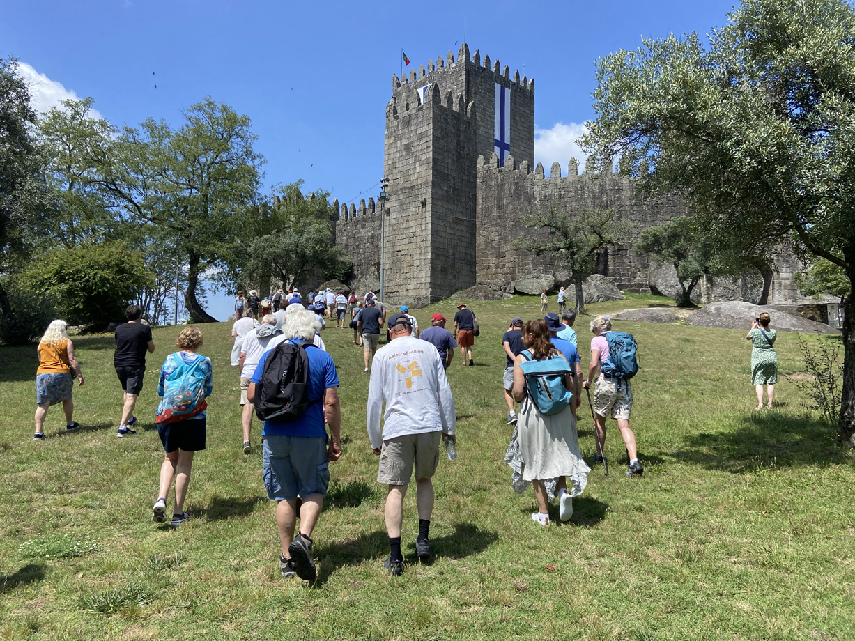 Men and women walk up a grassy hill to a historic stone castle in Guimares