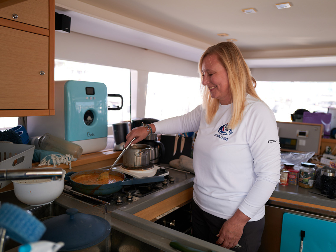 A woman cooks a meal in the galley of her catamaran Homecoming