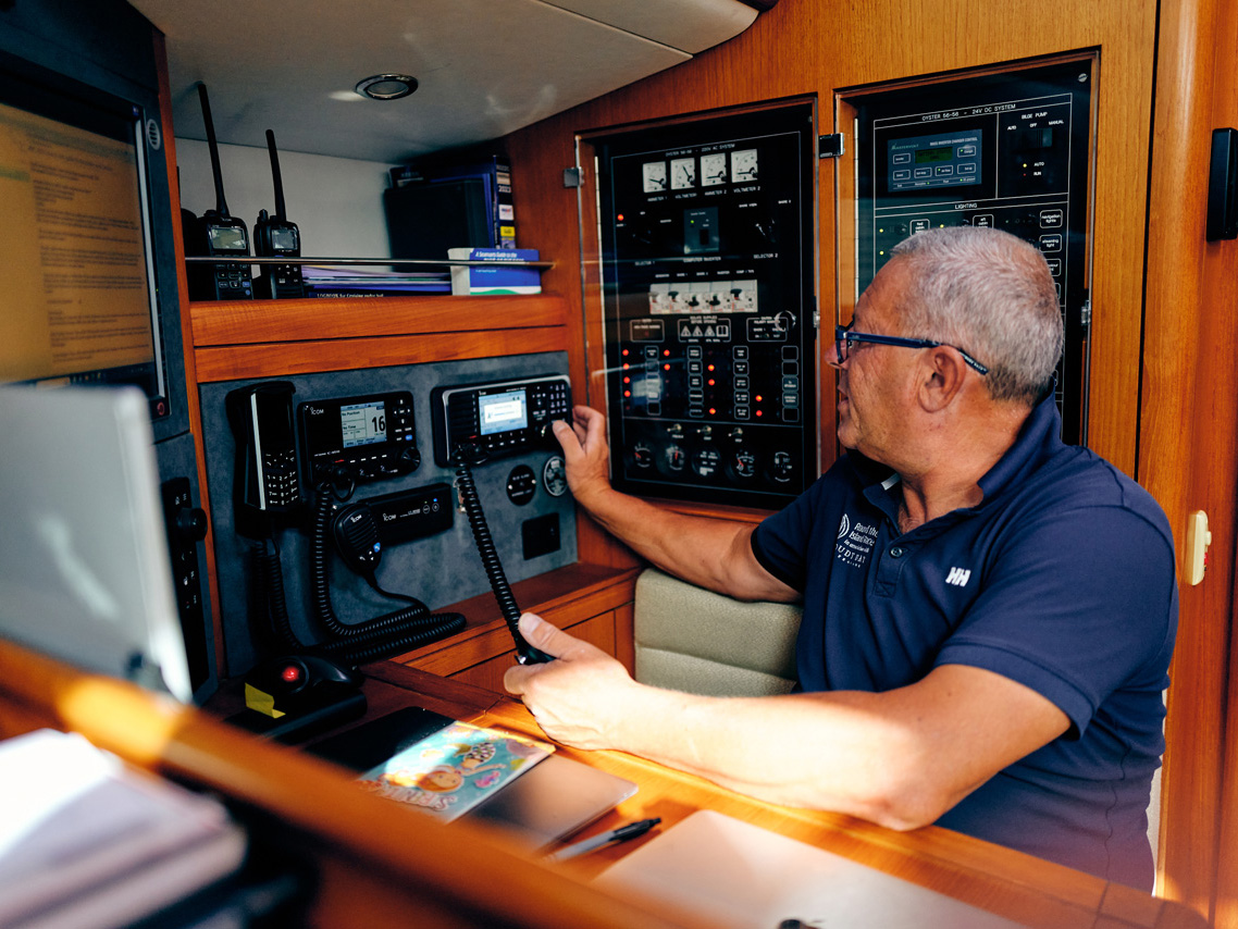 A man wearing a blue shirt sits at the navigation station of his yacht looking at an SSB radio