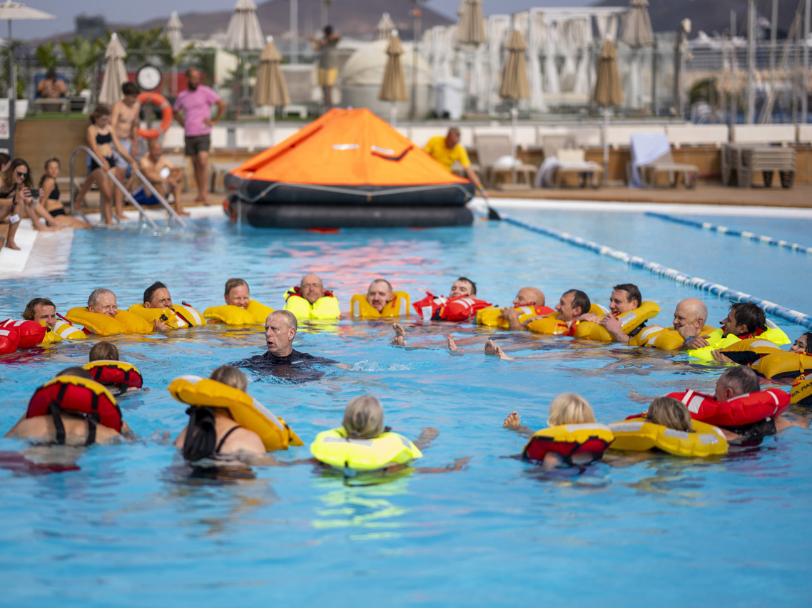 People wearing lifejackets form a circle in a swimming pool as part of the safety demonstration in Las Palmas
