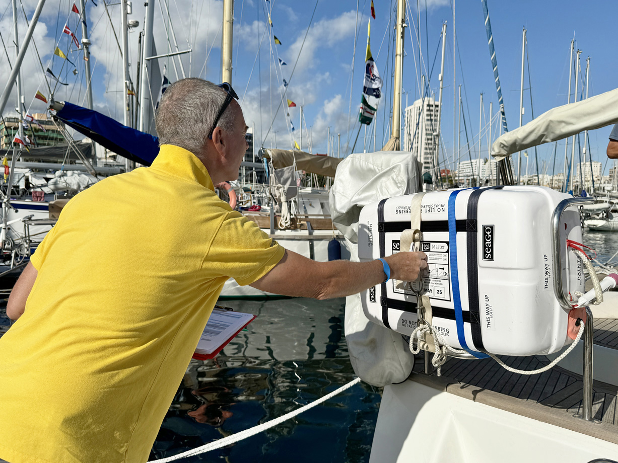 A man in a yellow shirt tests the fixing of a liferaft onboard at yacht at the start of ARC 2024