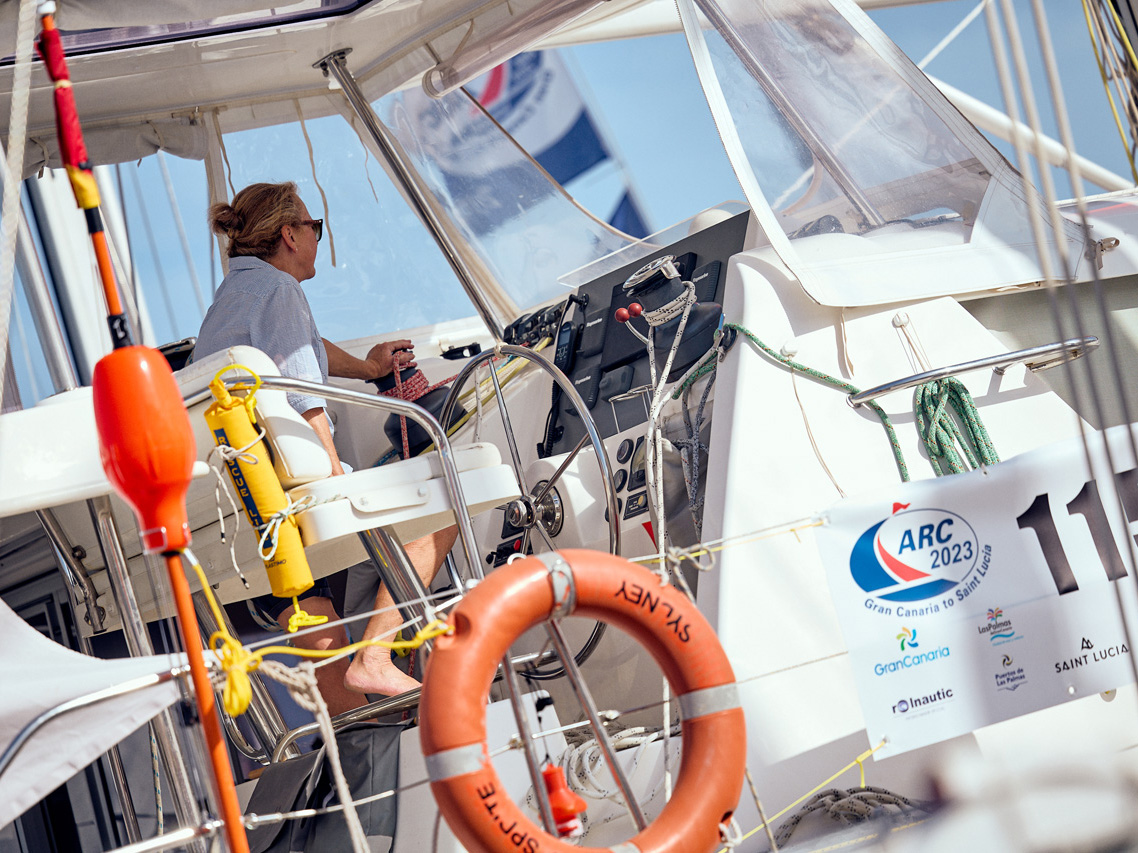 A woman drives a catamaran yacht with flags flying. Safety equipment is attached to the rails