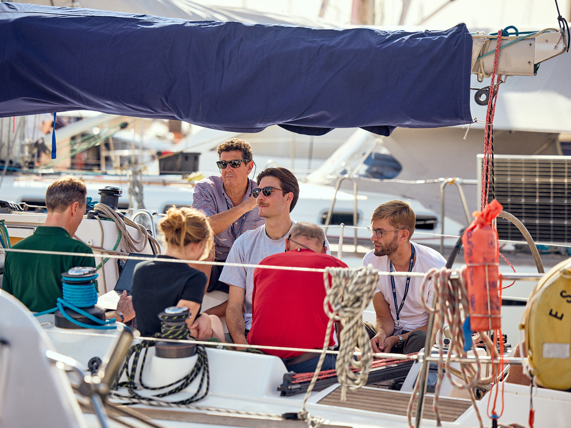 A group of young men and women sit talking in the cockpit of a yacht docked in Las Palmas Marina